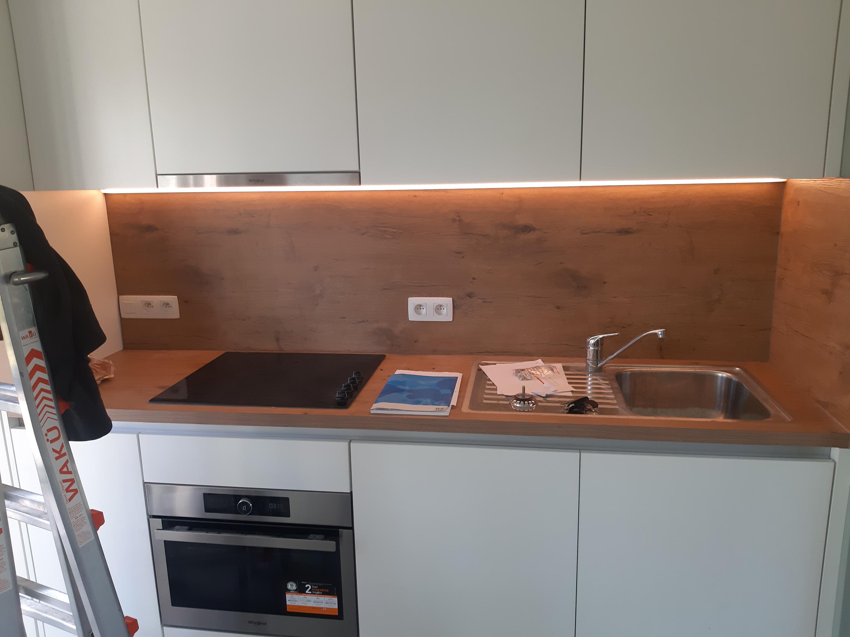 Doorlopende ledstrip onder de bovenkasten van een keuken, boven een houten achterwand met stopcontacten